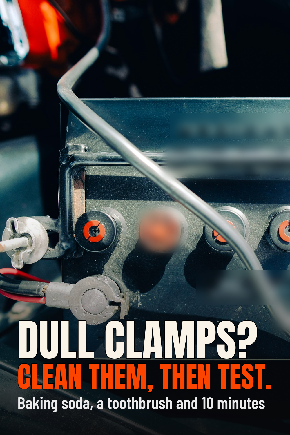 Battery terminal corrosion cleaning: close-up of a black lead-acid car battery in an engine bay with orange cell caps and dull oxidised cable clamps, brand lettering blurred, with the words Dull clamps? Clean them, then test.